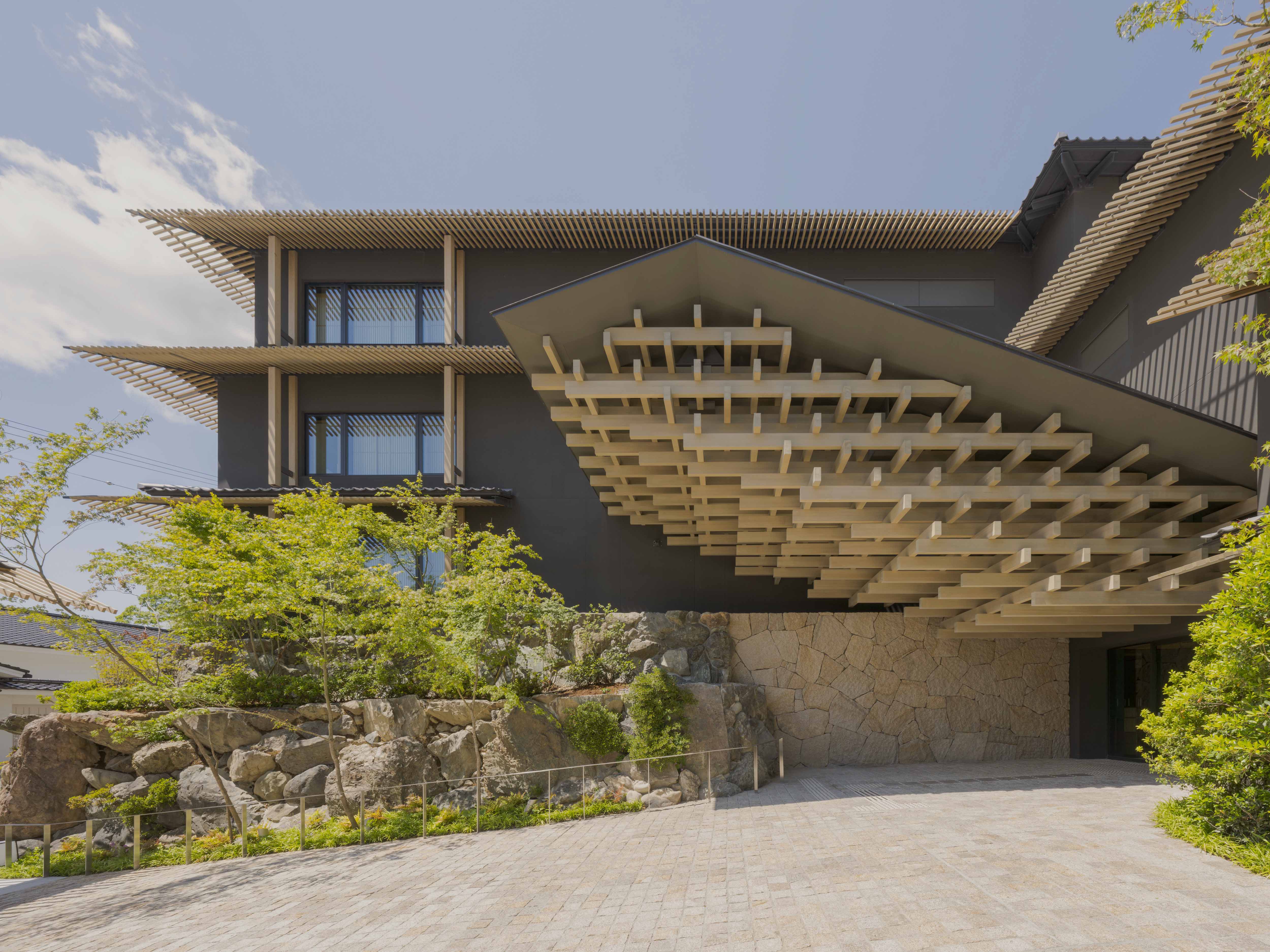 Modern building facade with wooden terrace amidst lush greenery at Banyan Tree Higashiyama Kyoto.